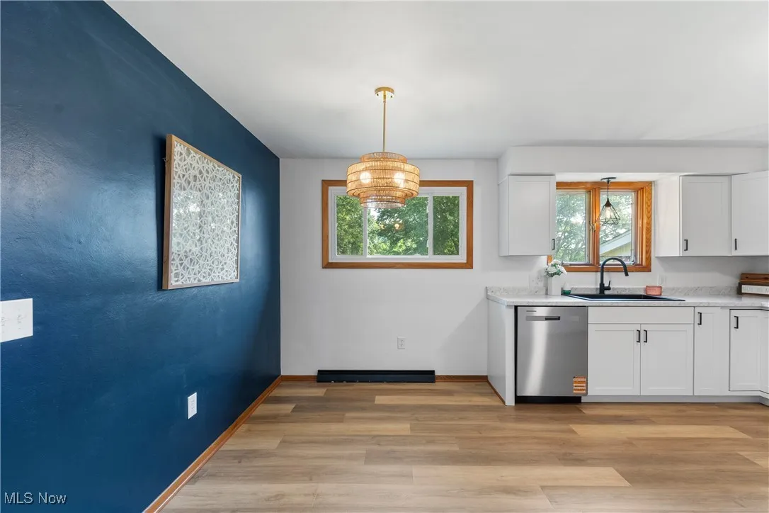 Kitchen featuring stainless steel dishwasher, white cabinetry, light countertops, and light wood-style floors