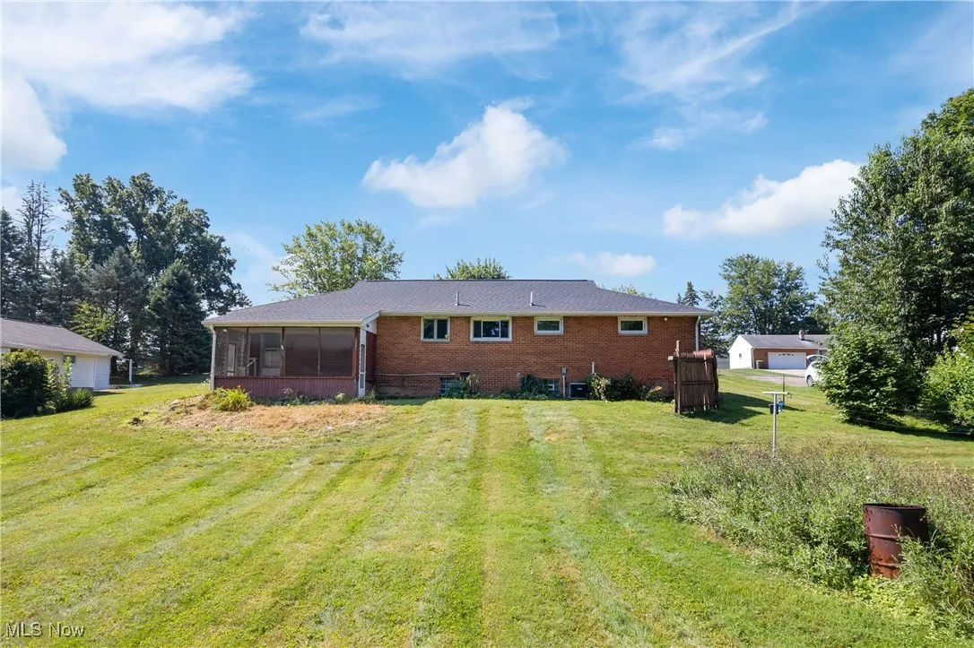 Back of property with a sunroom, a lawn, and brick siding