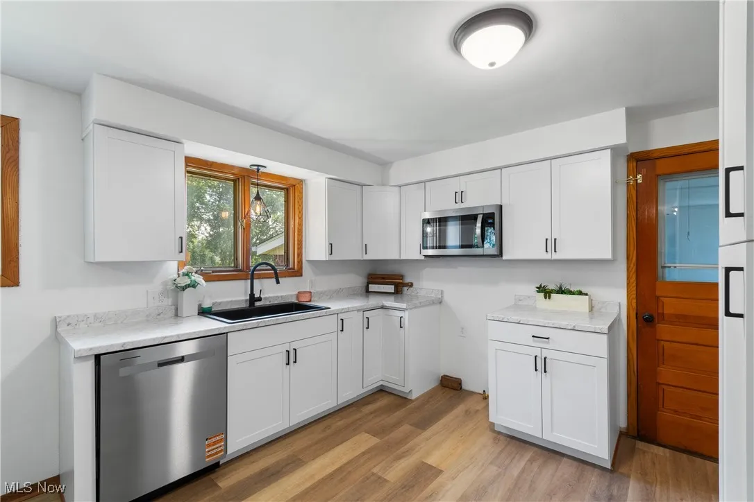Kitchen with stainless steel appliances, light wood-style flooring, and white cabinetry