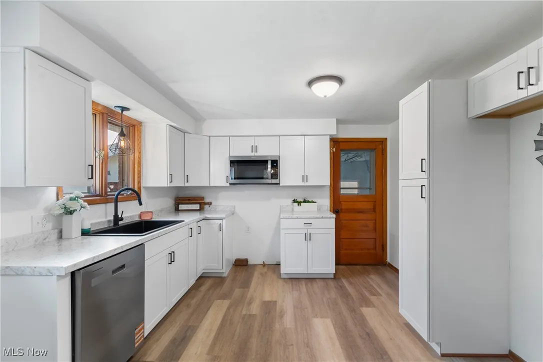 Kitchen with appliances with stainless steel finishes, light wood finished floors, and white cabinets
