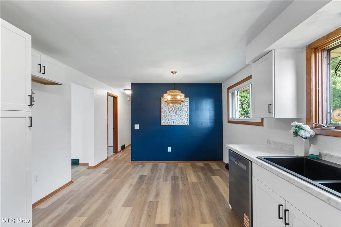 Kitchen with light wood-style floors, light countertops, dishwasher, white cabinets, and pendant lighting