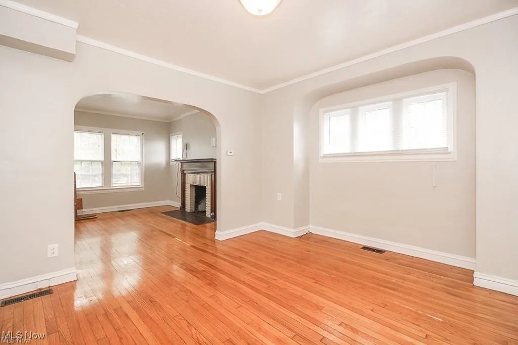 Unfurnished living room with crown molding, light wood-type flooring, a fireplace, and arched walkways