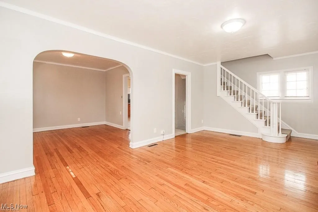 Empty room featuring arched walkways, light wood-type flooring, ornamental molding, and stairway