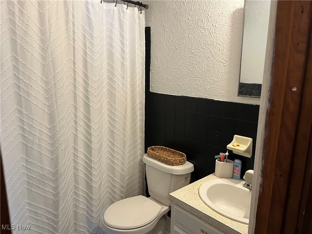 Bathroom with a textured wall, tile walls, vanity, wainscoting, and a shower with shower curtain