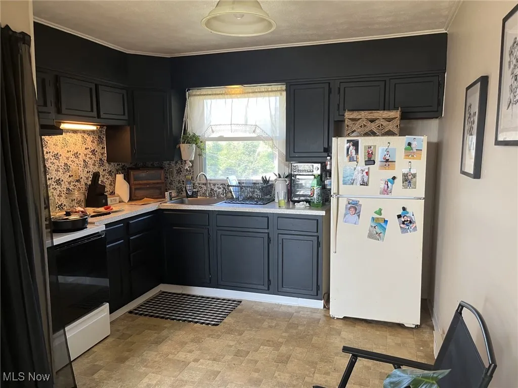 Kitchen with freestanding refrigerator, light countertops, electric range oven, crown molding, and decorative backsplash