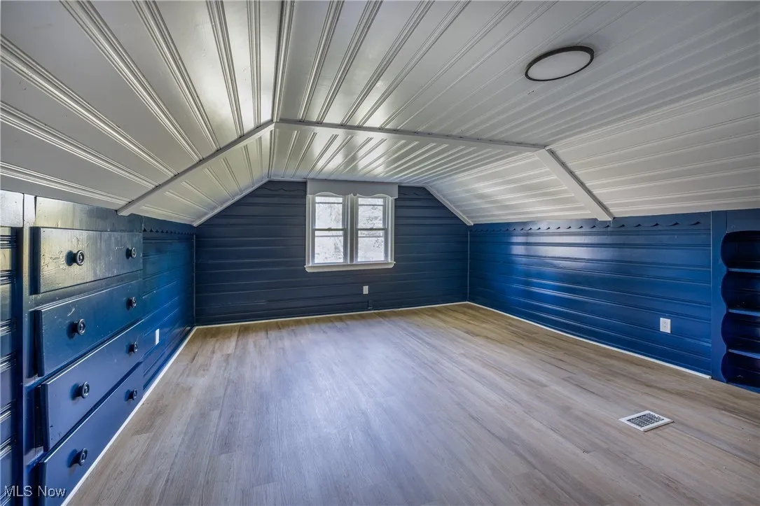 Bonus room featuring wood walls, wood finished floors, and vaulted ceiling