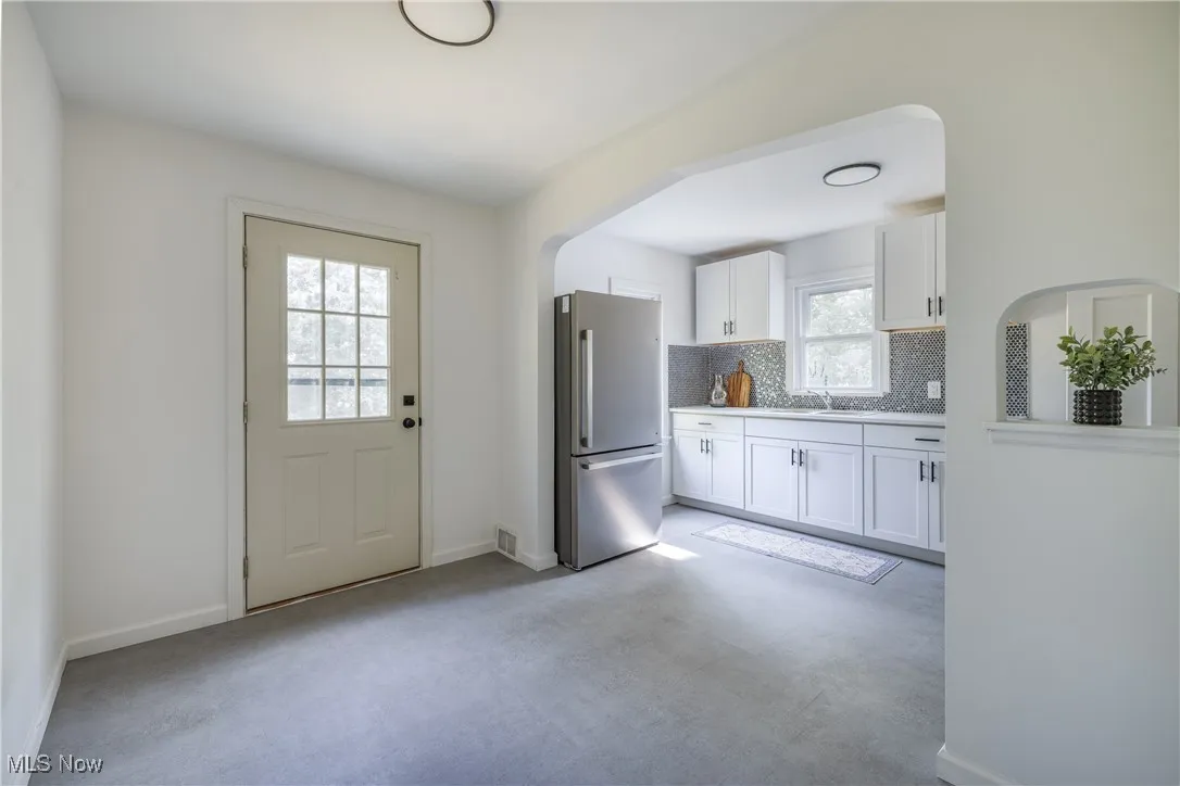 Kitchen with freestanding refrigerator, decorative backsplash, white cabinets, arched walkways, and light countertops
