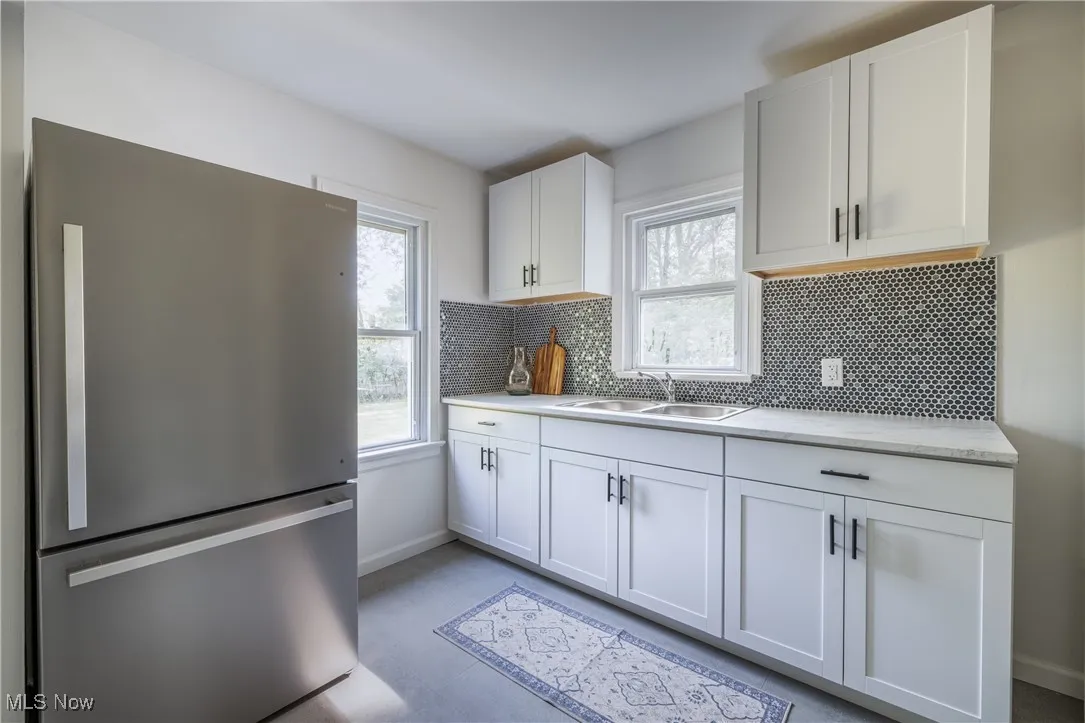 Kitchen with freestanding refrigerator, healthy amount of natural light, white cabinets, and decorative backsplash