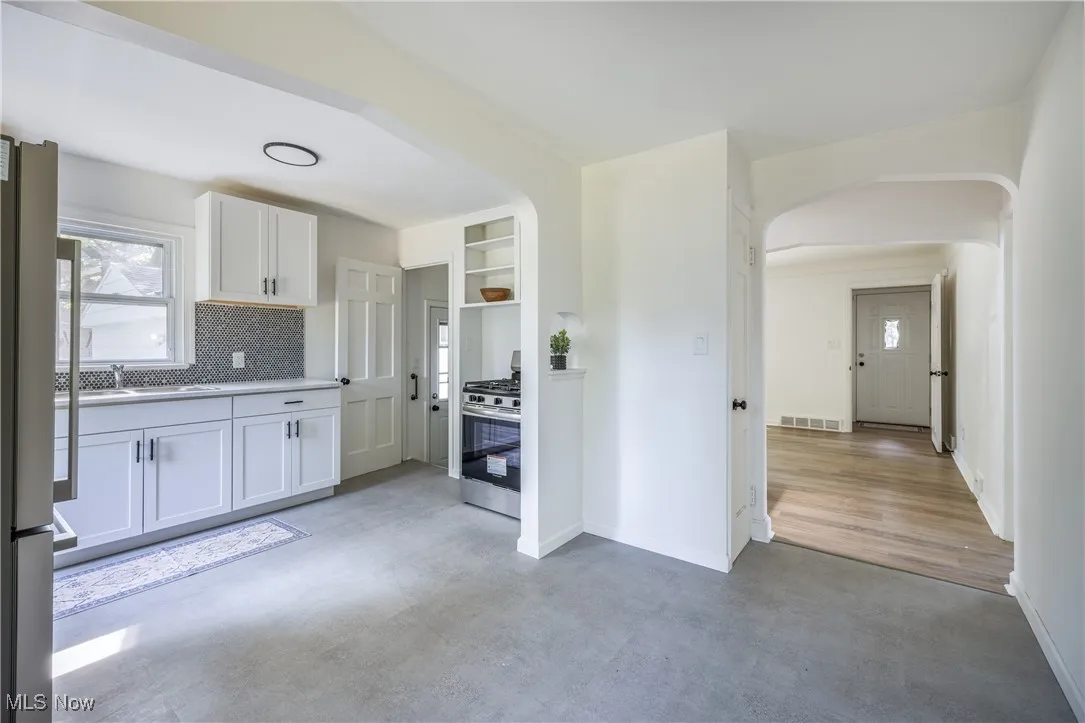 Kitchen featuring arched walkways, stainless steel range with gas stovetop, tasteful backsplash, freestanding refrigerator, and white cabinetry