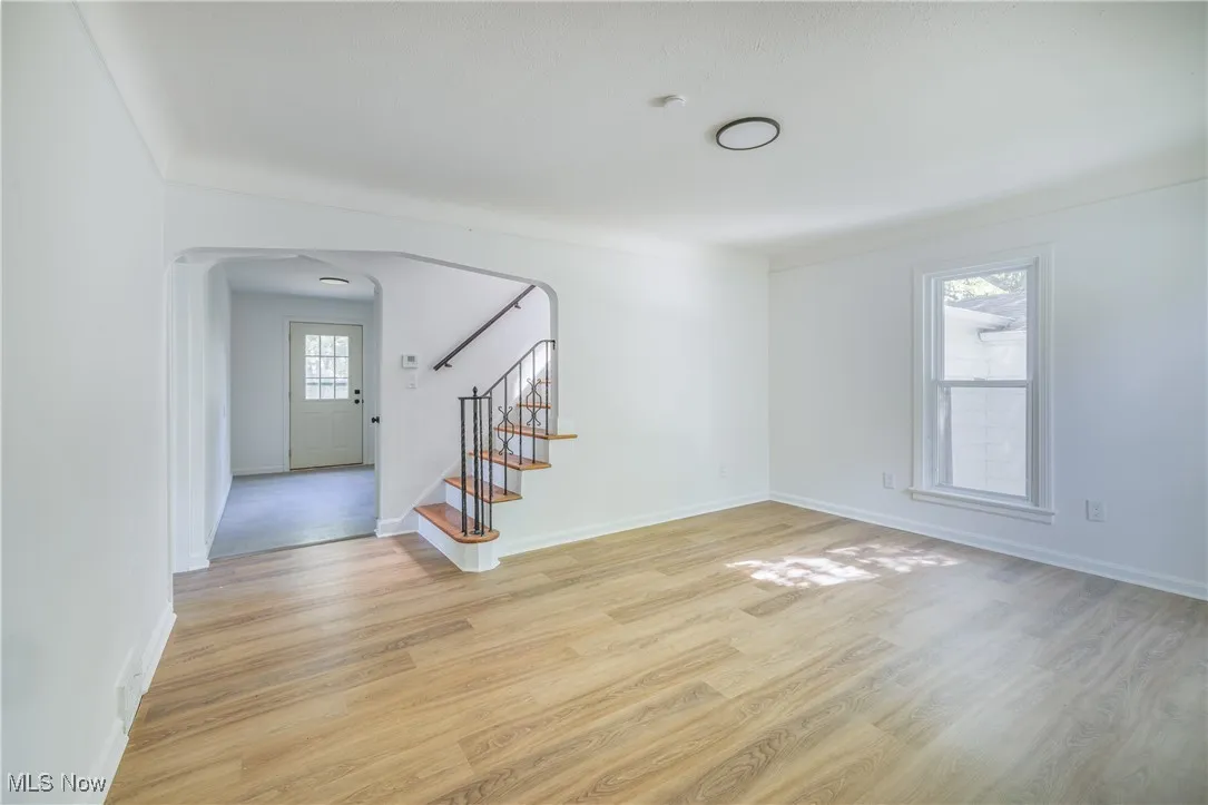 Empty room featuring arched walkways, light wood-style floors, stairway, and ornamental molding