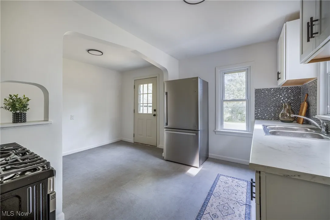 Kitchen with freestanding refrigerator, range with gas stovetop, tasteful backsplash, white cabinets, and arched walkways