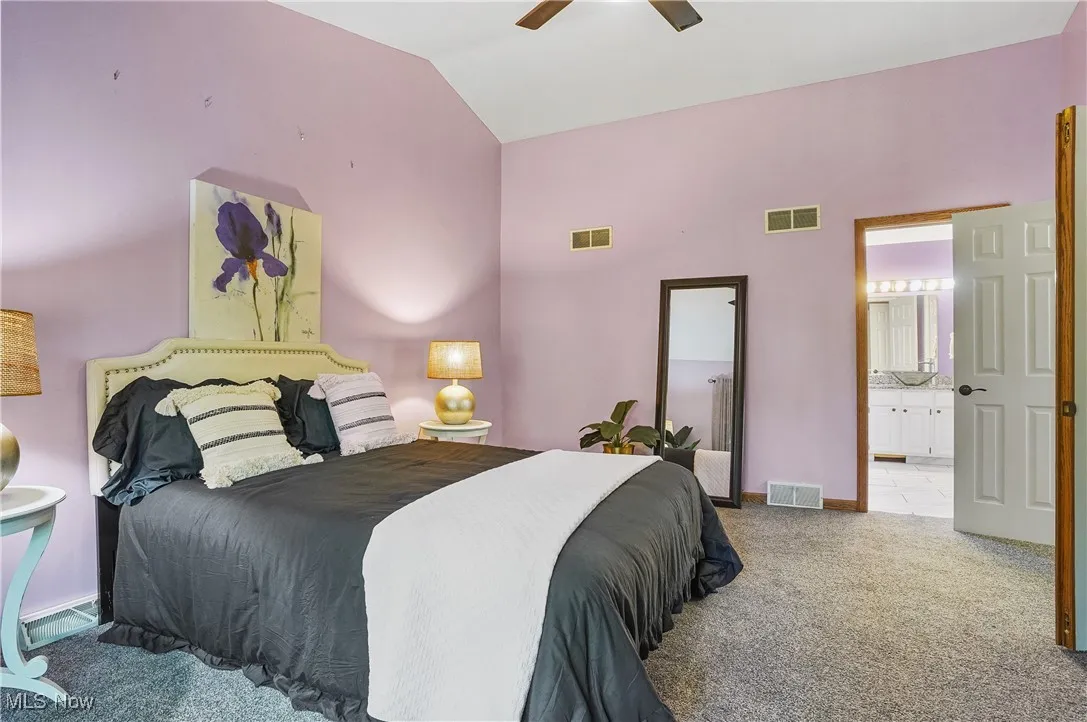 Bedroom featuring carpet floors, vaulted ceiling, connected bathroom, and ceiling fan