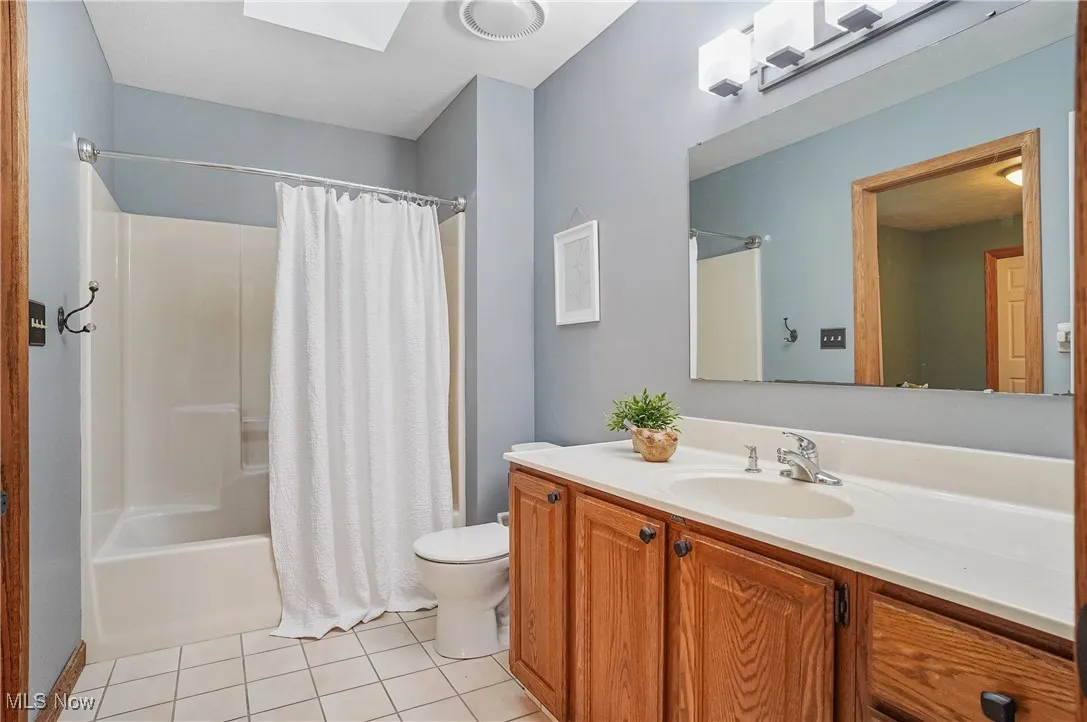 Full bath with tile patterned floors, shower / bath combo with shower curtain, vanity, and a skylight