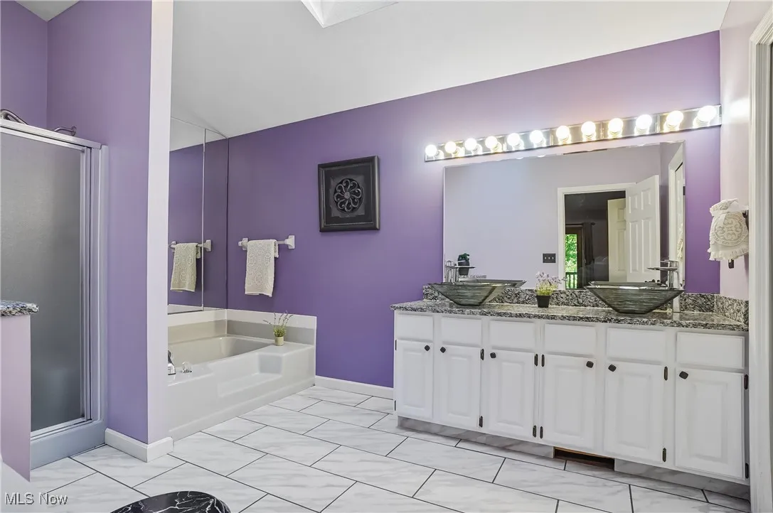 Bathroom featuring a stall shower, double vanity, a bath, and lofted ceiling