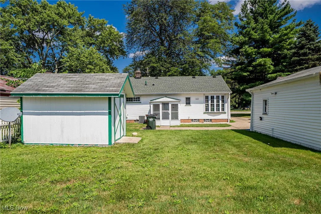 Back of property with a lawn, a shed, a chimney, and roof with shingles