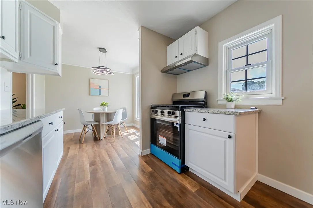 Kitchen with stainless steel appliances, healthy amount of natural light, exhaust hood, dark wood-style flooring, and crown molding