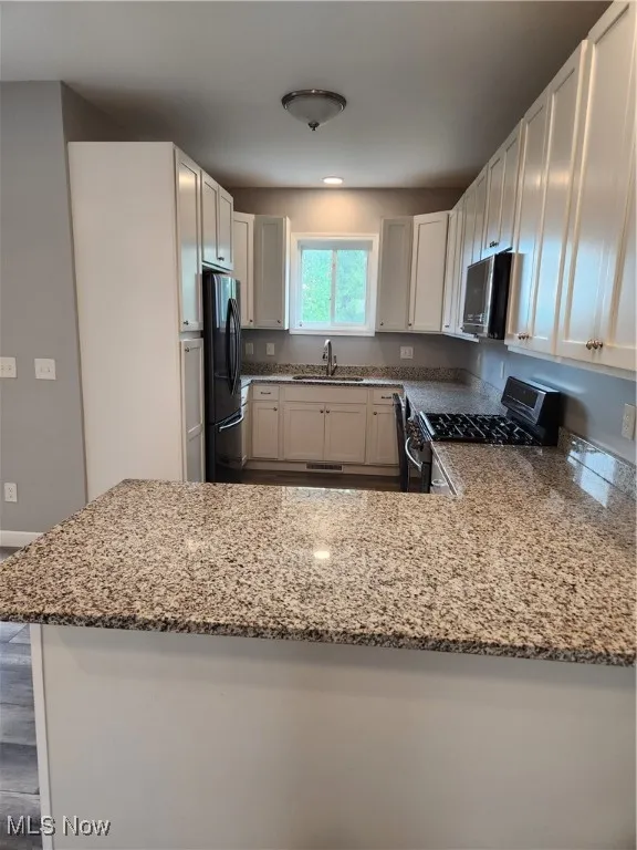 Kitchen featuring range, stone counters, fridge, and a peninsula