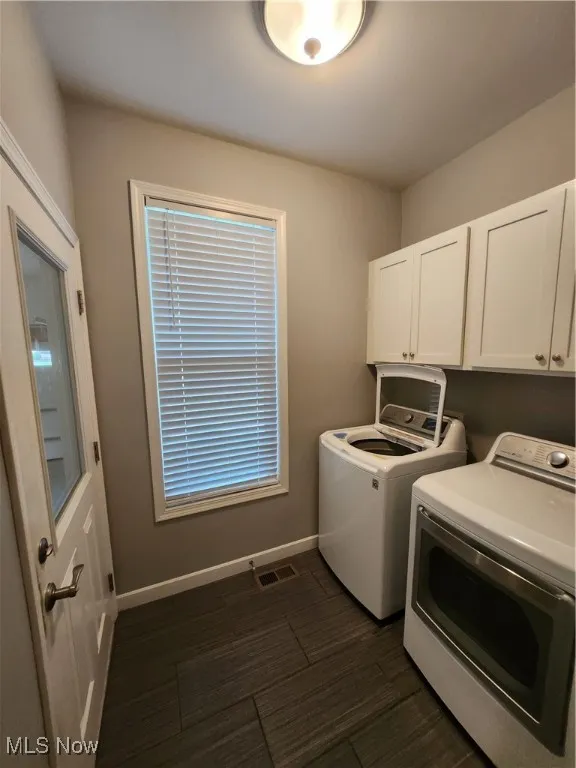 Laundry area featuring washing machine and clothes dryer, cabinet space, and dark wood-style floors