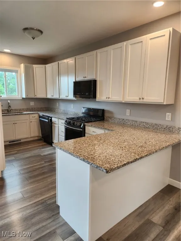 Kitchen with range with gas cooktop, dark wood-style flooring, a peninsula, light stone counters, and recessed lighting