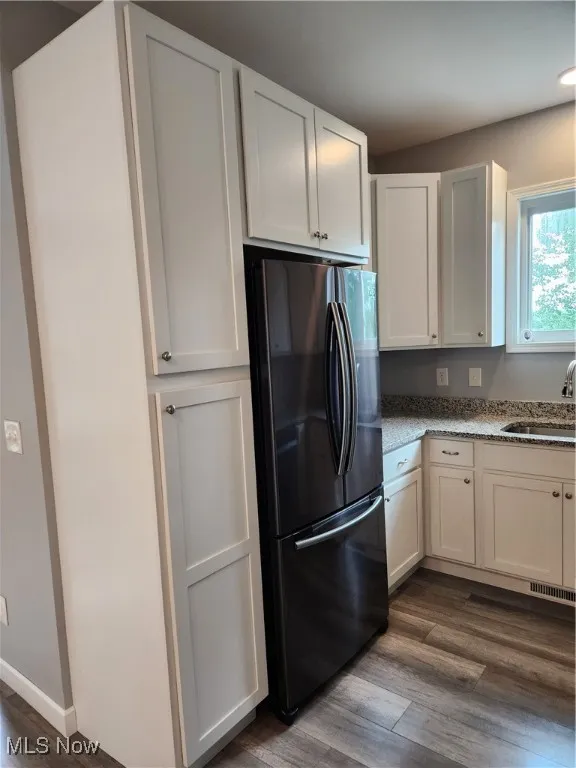 Kitchen featuring black refrigerator, dark wood-style flooring, light stone countertops, and white cabinetry