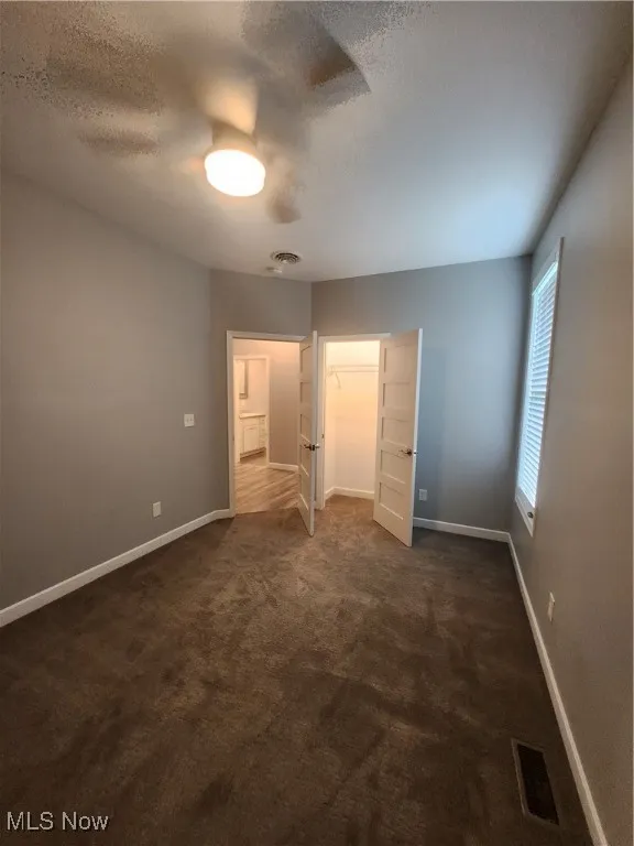 bedroom with dark colored carpet, a textured ceiling, a ceiling fan, and a spacious closet