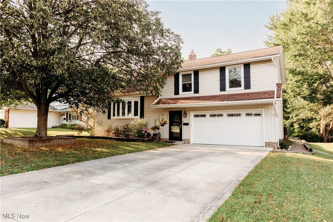 Tri-level home with a chimney, driveway, a garage, and a front lawn