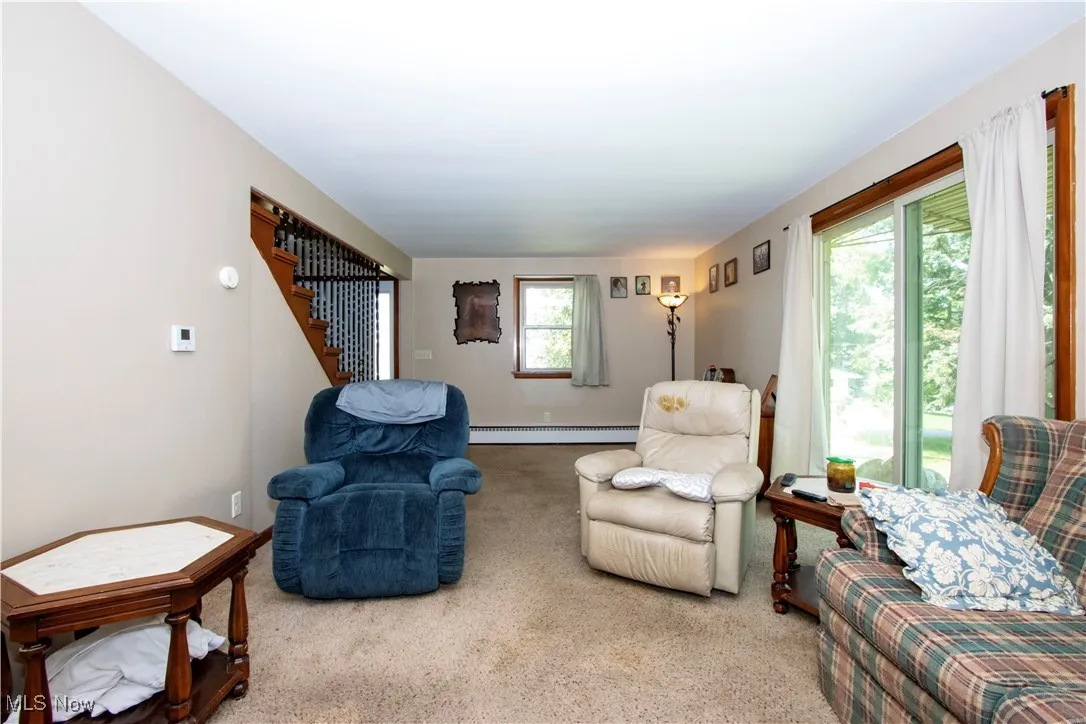 Living area with carpet flooring, stairway, and baseboard heating