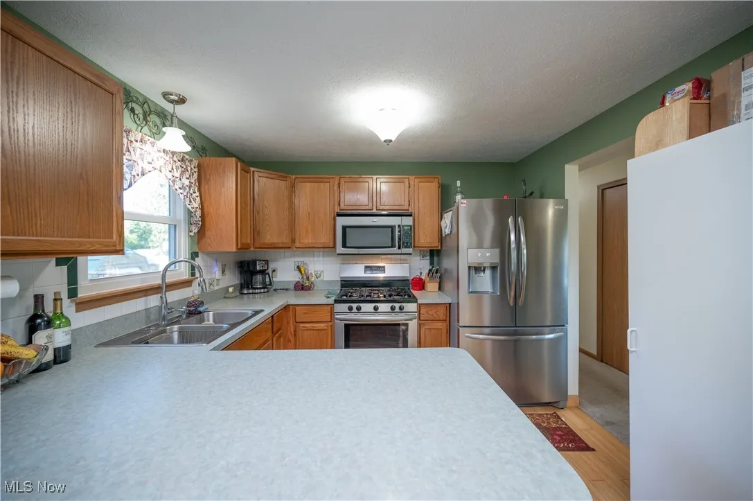 Kitchen featuring stainless steel appliances, decorative backsplash, light countertops, light wood-style floors, and a textured ceiling