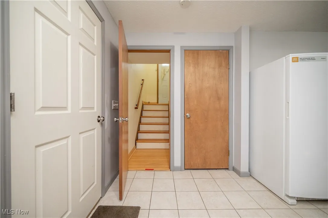 Hallway with a textured ceiling, stairway, and light tile patterned floors