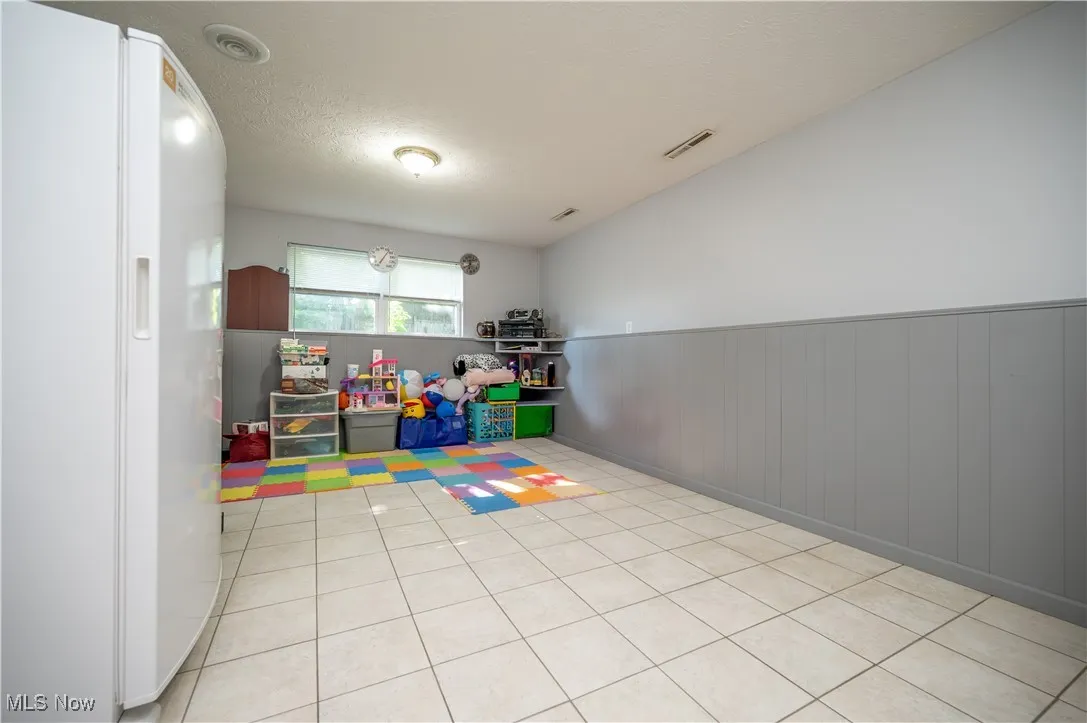 Game room with a wainscoted wall, a textured ceiling, light tile patterned floors, and wood walls