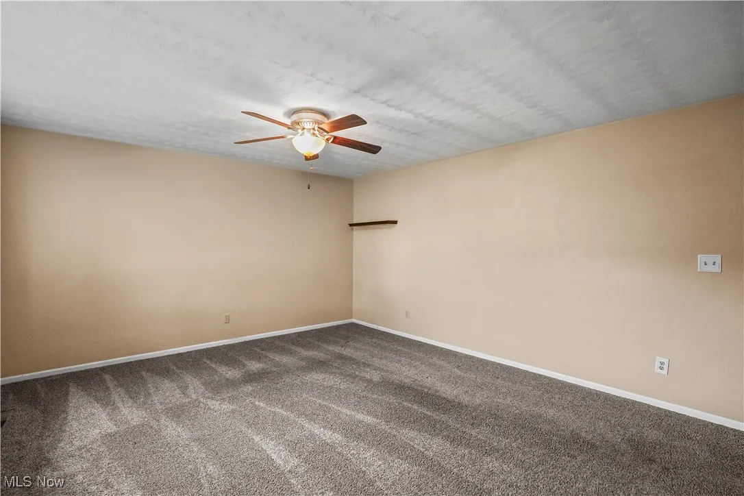 Unfurnished room with ceiling fan and dark colored carpet