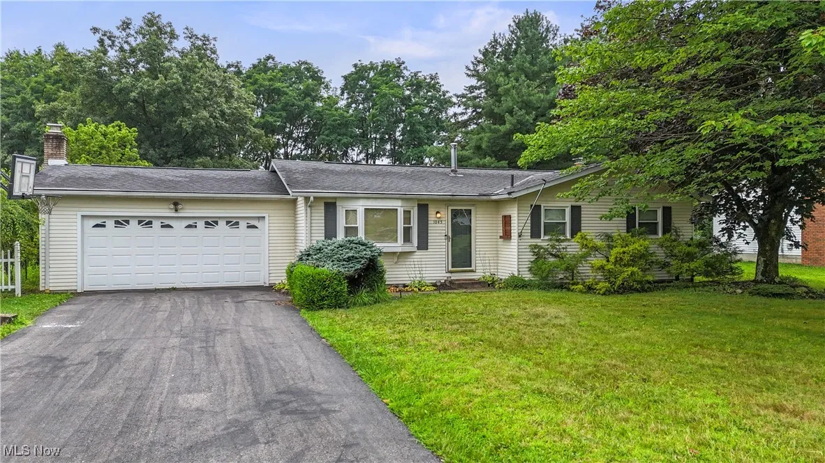 Ranch-style home featuring asphalt driveway, a chimney, a garage, and a front yard