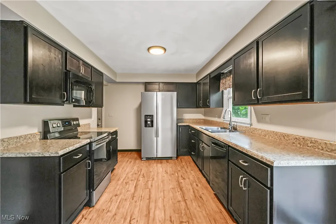 Kitchen with black appliances, light wood finished floors, light countertops, and dark cabinets