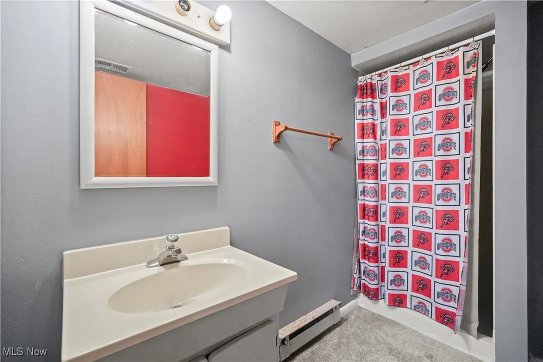 Full bath featuring a baseboard radiator, vanity, and curtained shower