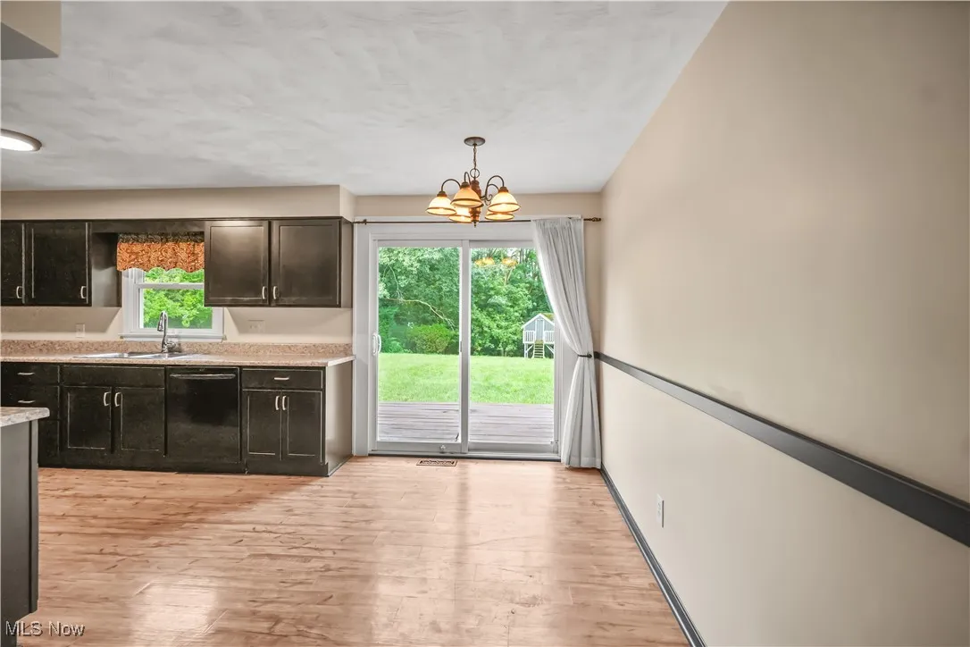 Kitchen featuring light wood finished floors, a chandelier, black dishwasher, decorative light fixtures, and a textured ceiling