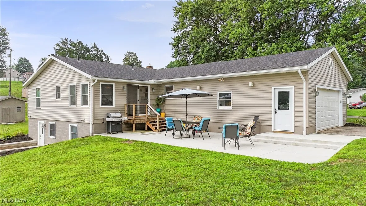 Back of house featuring an outdoor structure, a yard, roof with shingles, a patio area, and a chimney