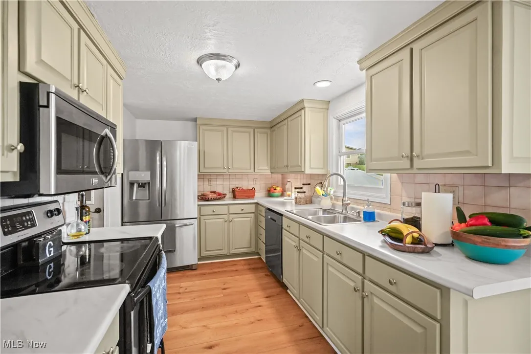 Kitchen featuring cream cabinets, stainless steel appliances, light countertops, light wood-style flooring, and tasteful backsplash