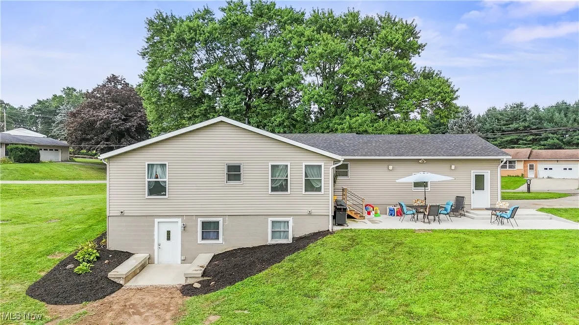 Rear view of property featuring a yard, a patio, roof with shingles, and view of scattered trees