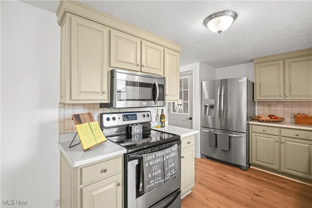 Kitchen featuring cream cabinetry, stainless steel appliances, light countertops, decorative backsplash, and a textured ceiling