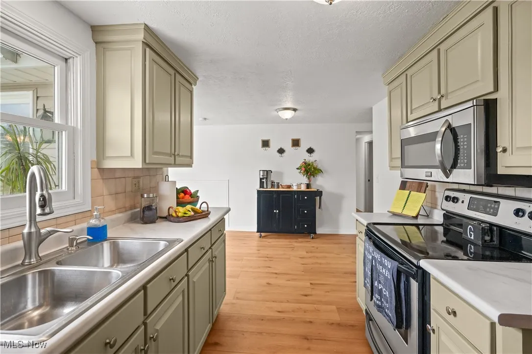 Kitchen with stainless steel appliances, decorative backsplash, cream cabinets, light wood-style floors, and a textured ceiling
