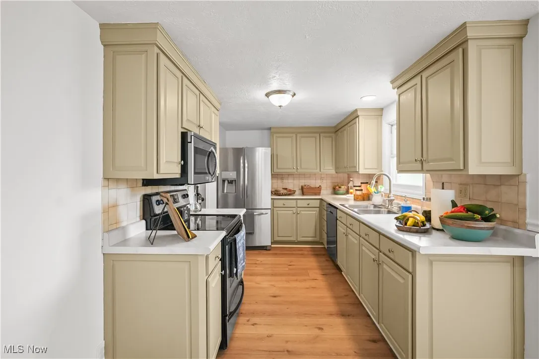 Kitchen with cream cabinetry, appliances with stainless steel finishes, decorative backsplash, light countertops, and light wood-style floors