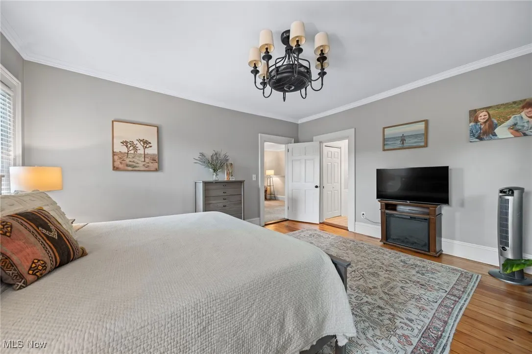 Bedroom with ornamental molding, a chandelier, and wood finished floors