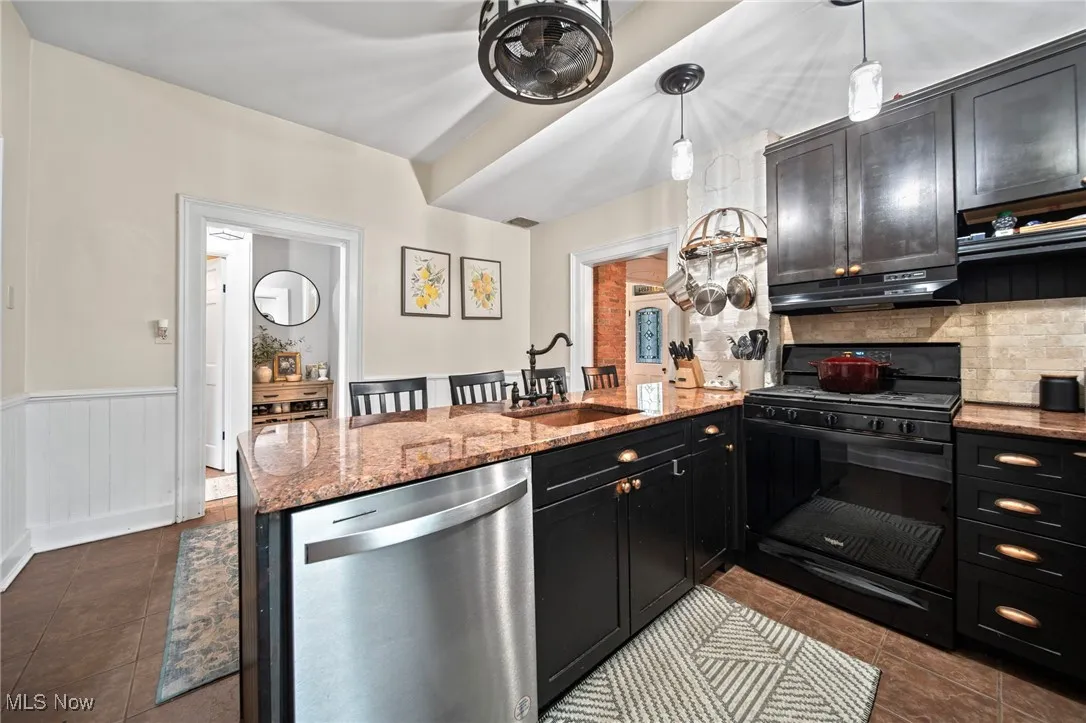 Kitchen with dark cabinetry, stainless steel dishwasher, black range with gas stovetop, a peninsula, and a wainscoted wall
