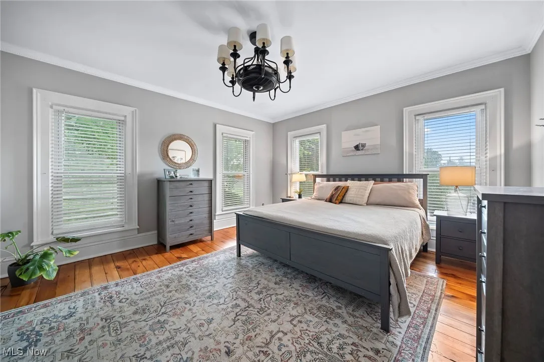 Bedroom featuring hardwood / wood-style flooring, a chandelier, crown molding, and multiple windows
