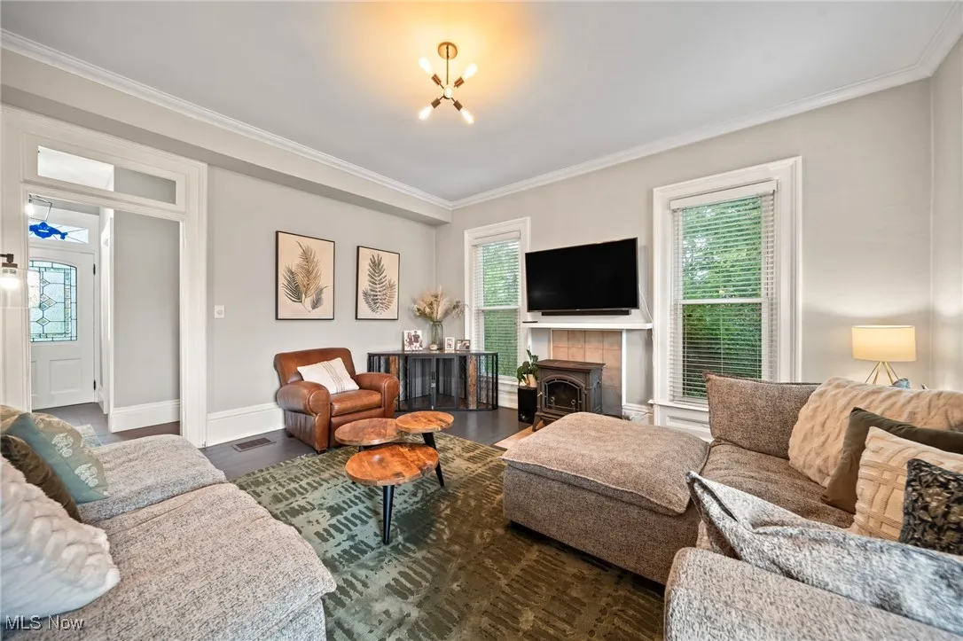 Living room with healthy amount of natural light, a chandelier, crown molding, dark wood-style flooring, and a wood stove