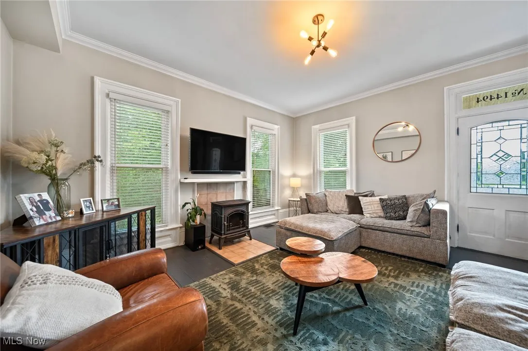 Living room featuring a wood stove, crown molding, wood finished floors, and a chandelier