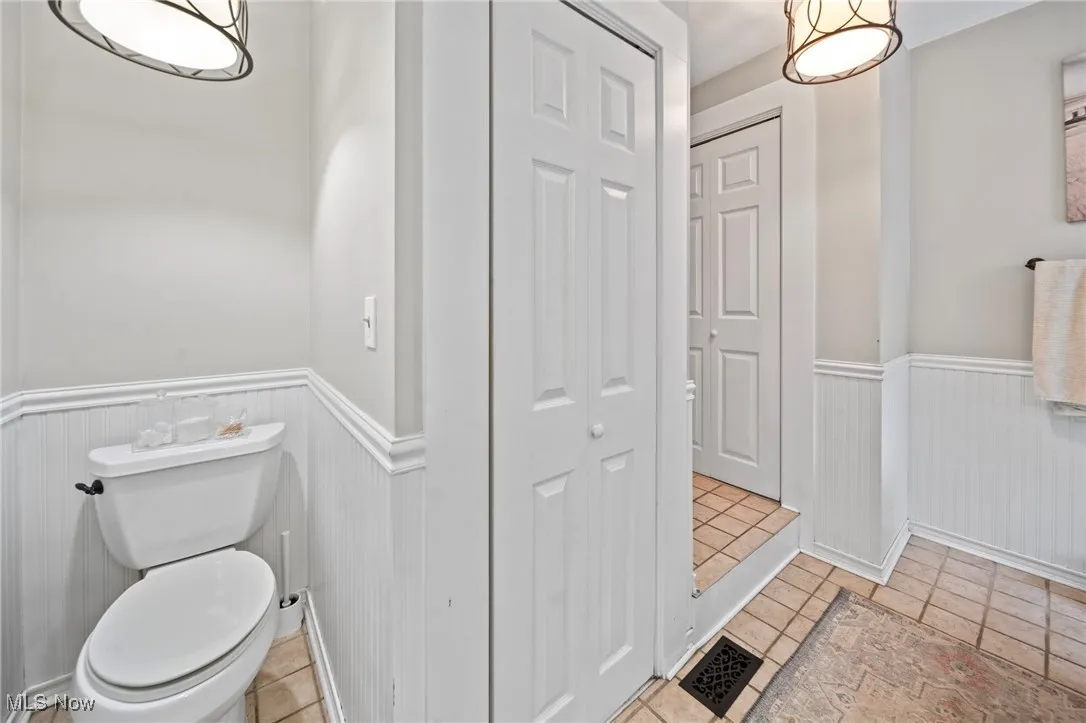 Bathroom featuring a wainscoted wall, a closet, tile patterned floors, and a decorative wall