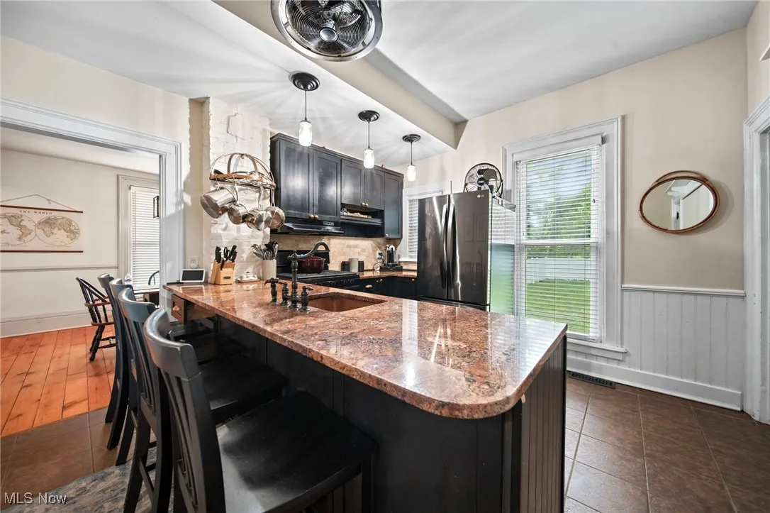 Kitchen with freestanding refrigerator, a peninsula, dark stone countertops, a kitchen bar, and decorative light fixtures