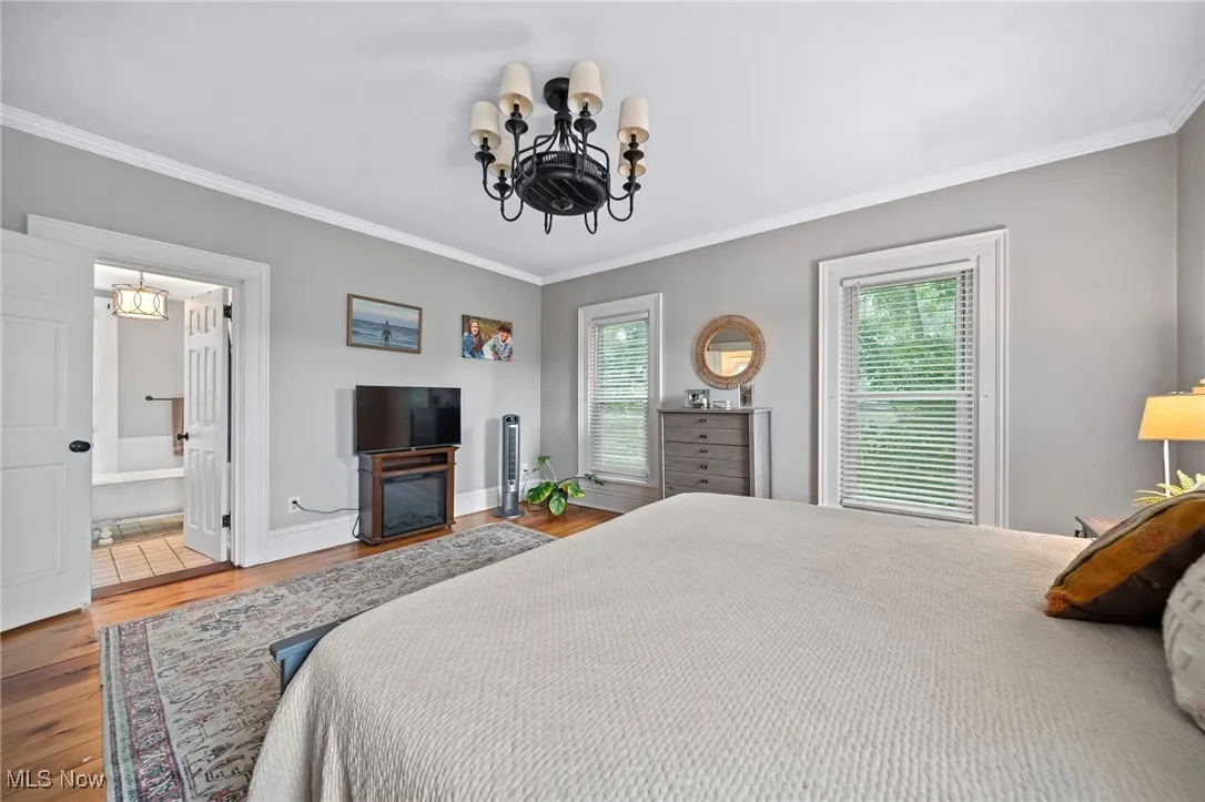 Bedroom with a chandelier, ornamental molding, wood finished floors, and ensuite bathroom