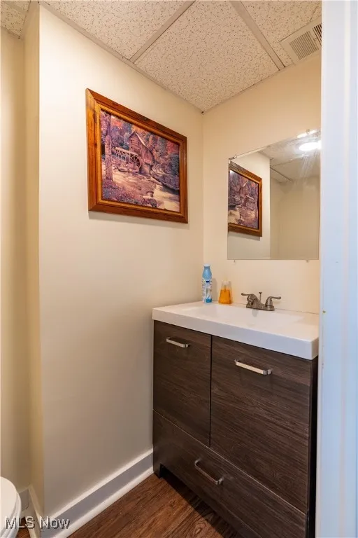 Bathroom with a drop ceiling, toilet, vanity, and hardwood / wood-style floors